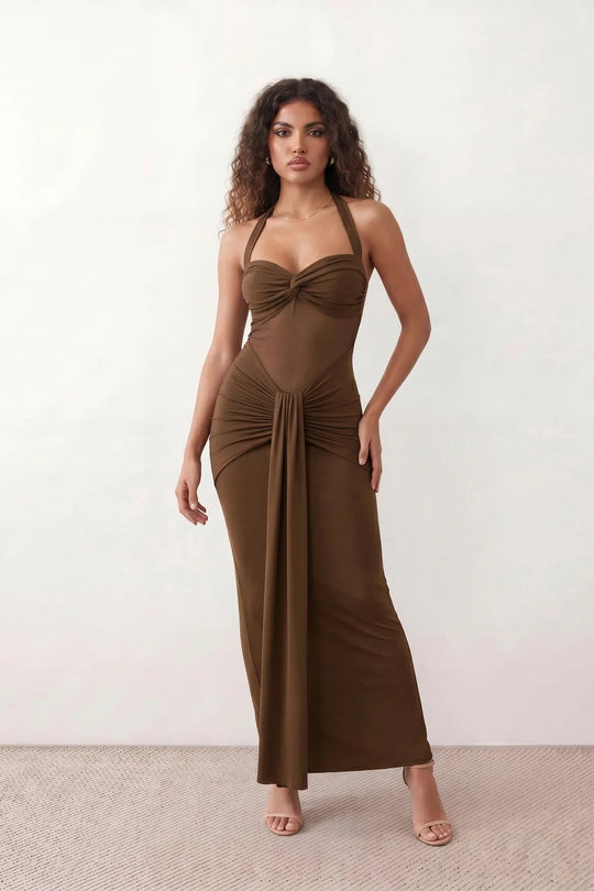 Woman wearing the Halter Neck Mermaid Maxi Dress featuring a sweetheart twist-knot neckline, sheer mesh waist panel, ruched mermaid silhouette, draped front skirt, open back with halter tie fastening, and elegant floor-length finish.