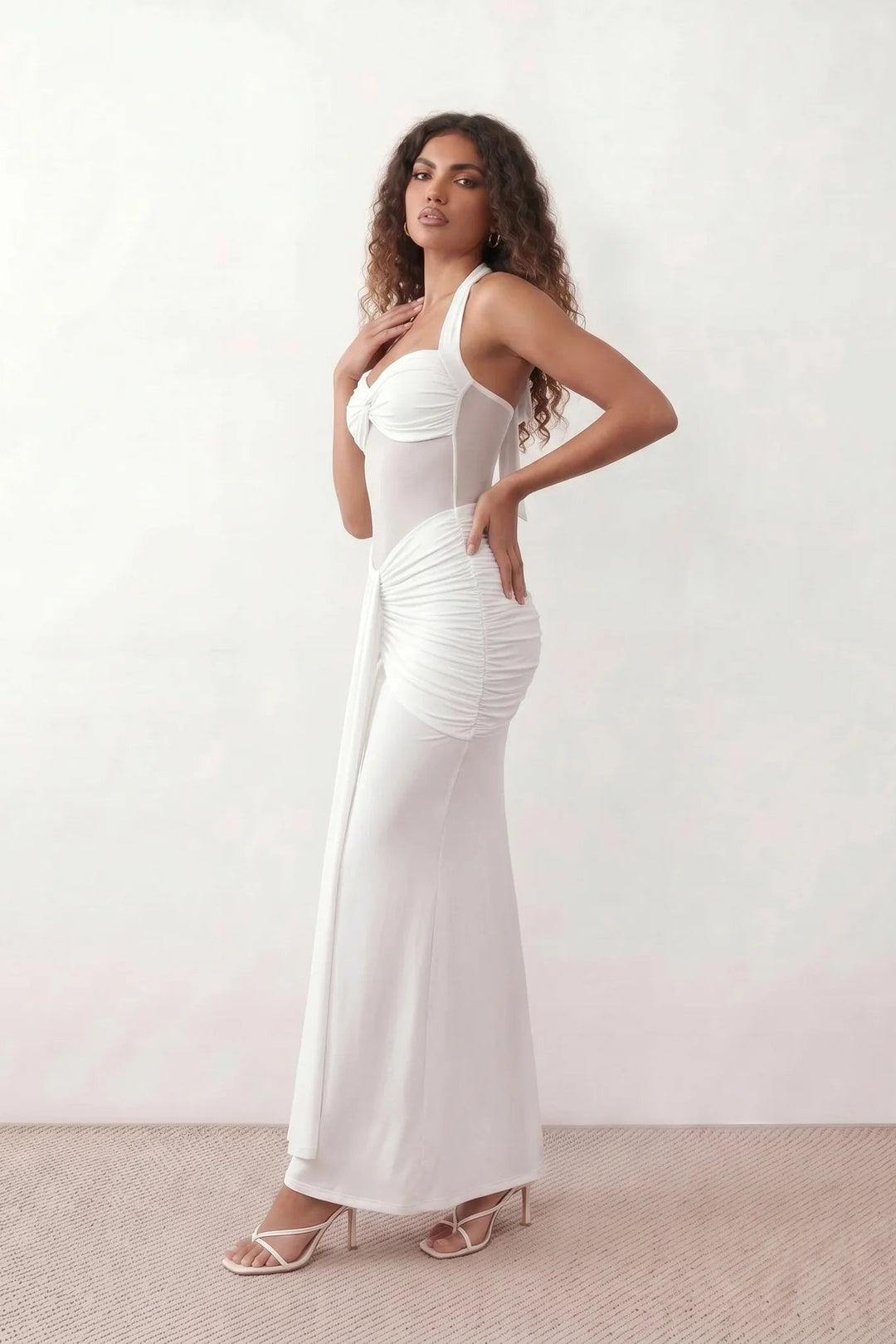 Woman wearing the Halter Neck Mermaid Maxi Dress featuring a sweetheart twist-knot neckline, sheer mesh waist panel, ruched mermaid silhouette, draped front skirt, open back with halter tie fastening, and elegant floor-length finish.