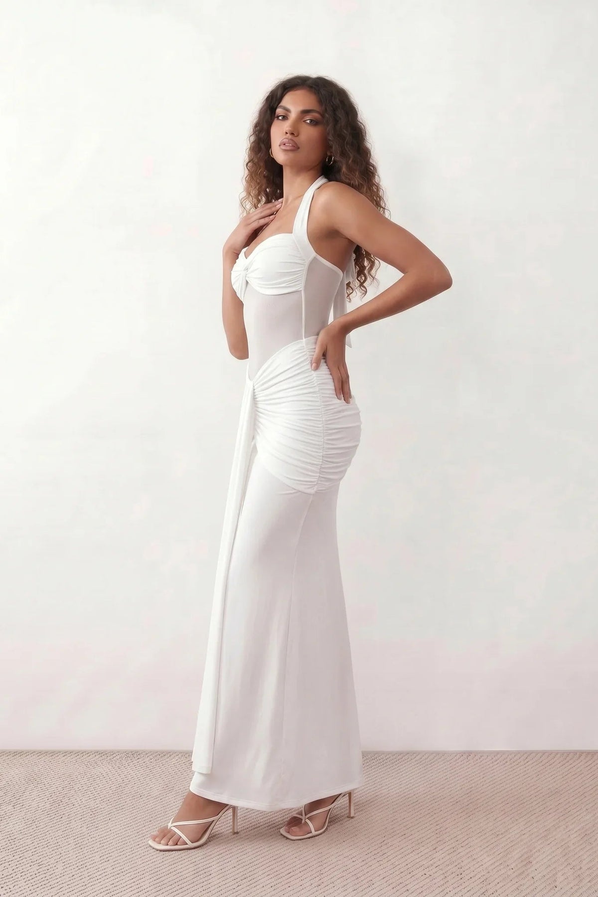 Woman wearing the Halter Neck Mermaid Maxi Dress featuring a sweetheart twist-knot neckline, sheer mesh waist panel, ruched mermaid silhouette, draped front skirt, open back with halter tie fastening, and elegant floor-length finish.