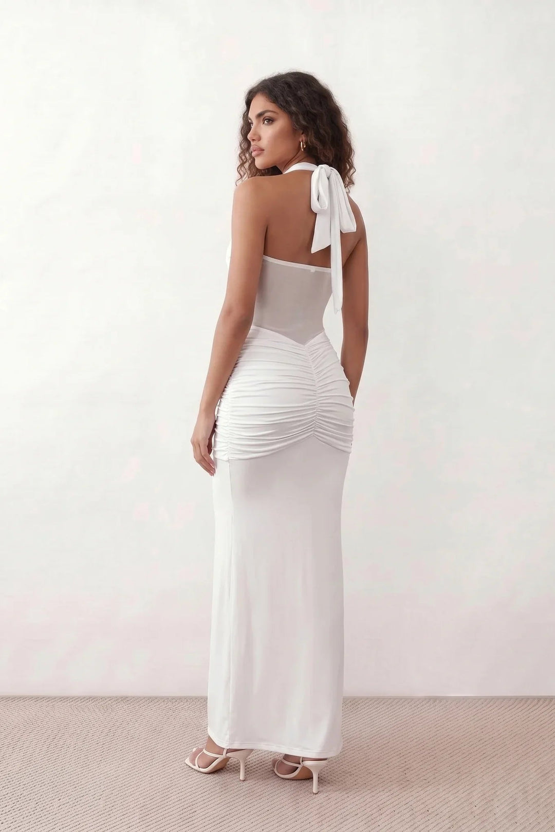 Woman wearing the Halter Neck Mermaid Maxi Dress featuring a sweetheart twist-knot neckline, sheer mesh waist panel, ruched mermaid silhouette, draped front skirt, open back with halter tie fastening, and elegant floor-length finish.