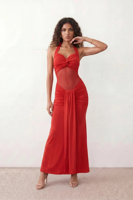 Woman wearing the Halter Neck Mermaid Maxi Dress featuring a sweetheart twist-knot neckline, sheer mesh waist panel, ruched mermaid silhouette, draped front skirt, open back with halter tie fastening, and elegant floor-length finish.