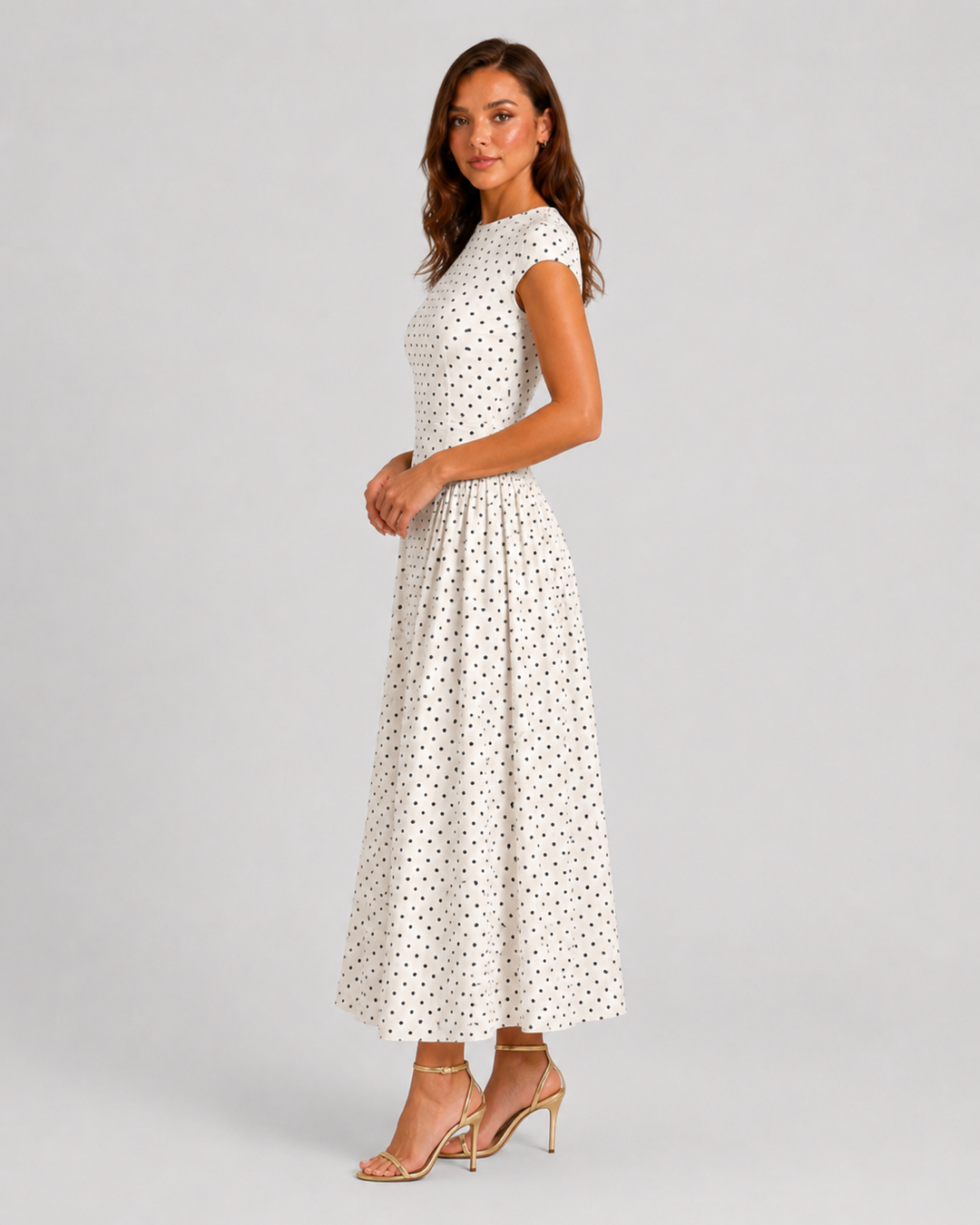 Woman wearing a polka dot maxi dress with a fitted bodice, cap sleeves, high neckline, and flowing pleated A-line skirt for elegant occasion wear.