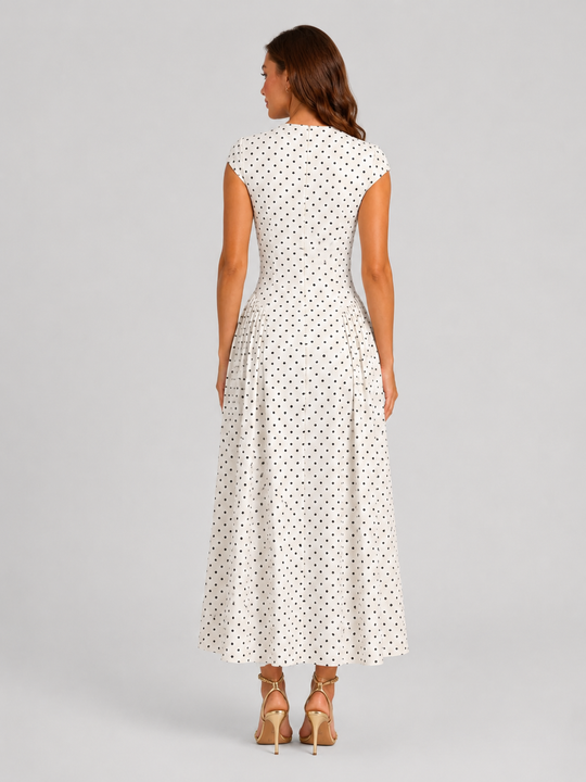 Woman wearing a polka dot maxi dress with a fitted bodice, cap sleeves, high neckline, and flowing pleated A-line skirt for elegant occasion wear.