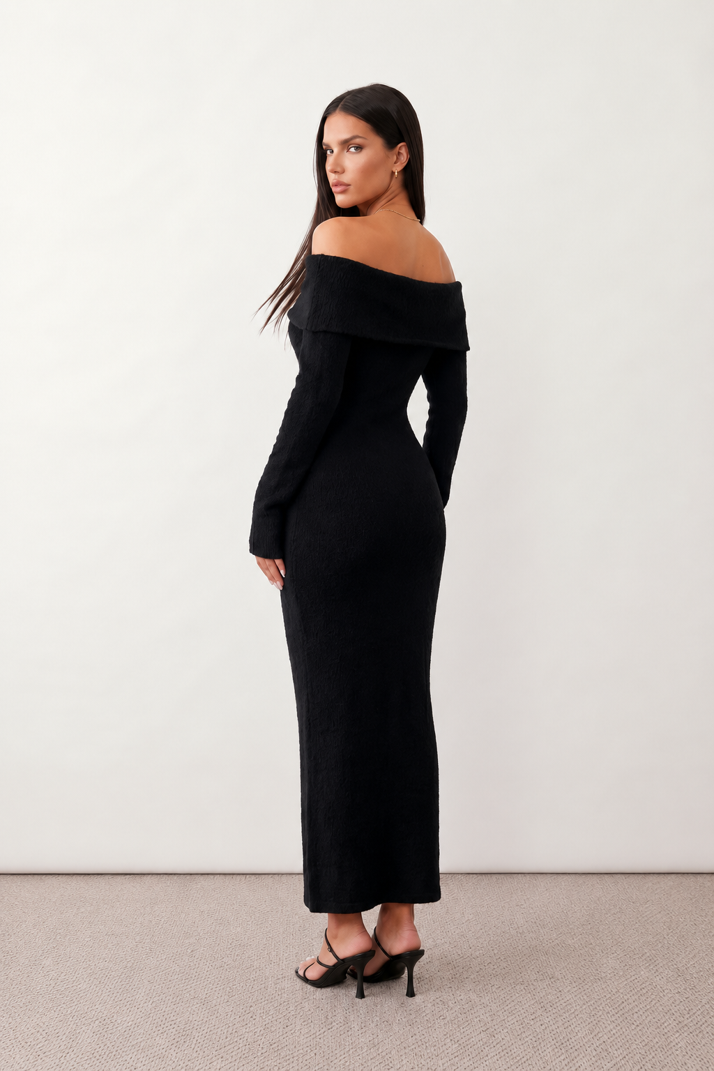 Woman wearing the Iustina Off Shoulder Fitted Maxi Dress featuring a Bardot neckline, soft draped shoulders, full-length sleeves, textured stretch knit fabric and a fitted floor-length silhouette, ideal for formal occasions and evening events.