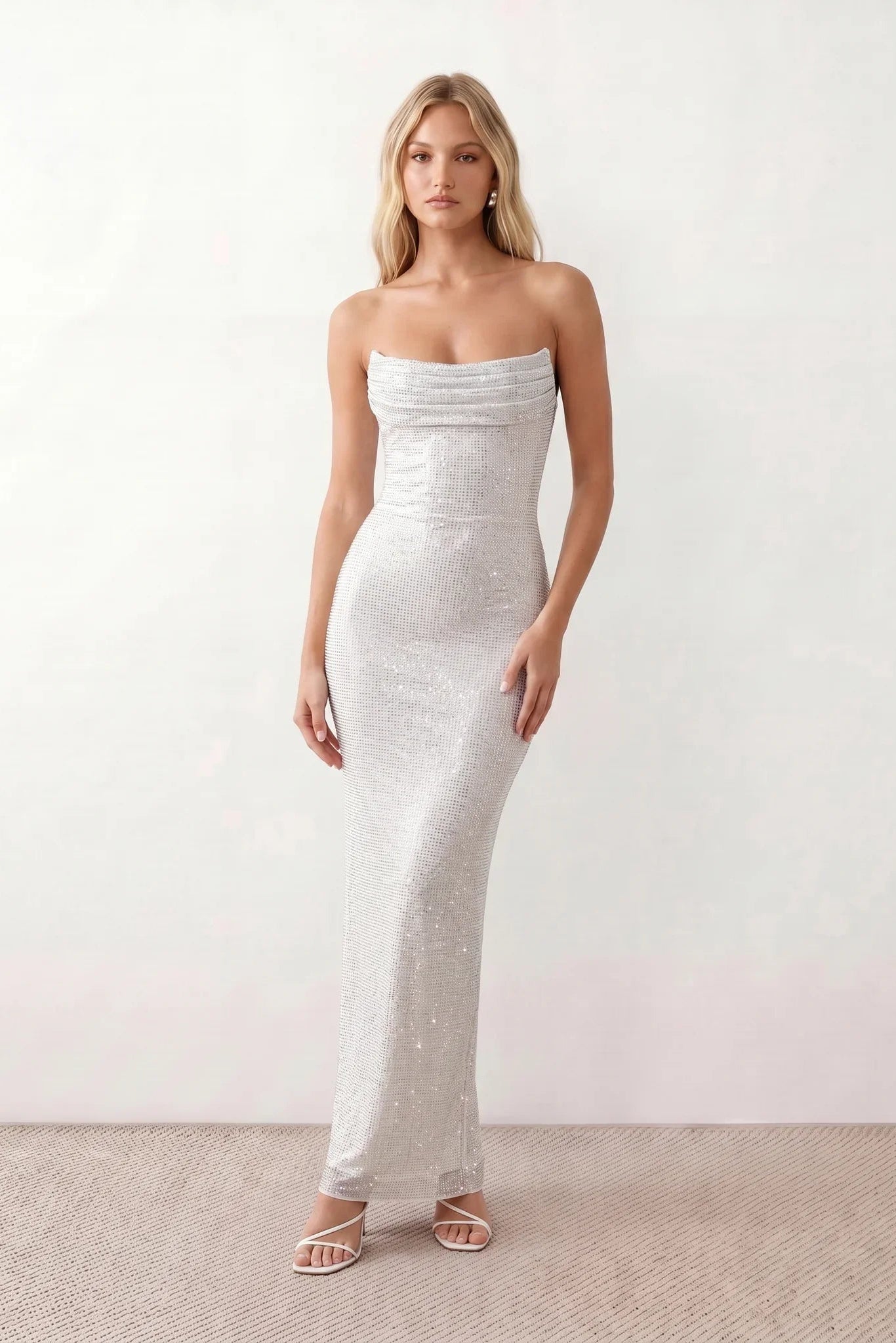 Woman wearing the Izabela sequined strapless maxi dress featuring shimmering all-over sequins, sparkling rhinestone embellishments, a ruched cowl-fold bust, adjustable lace-up corset back and a figure-skimming column silhouette with a floor-length hem, perfect for formal evening occasions.