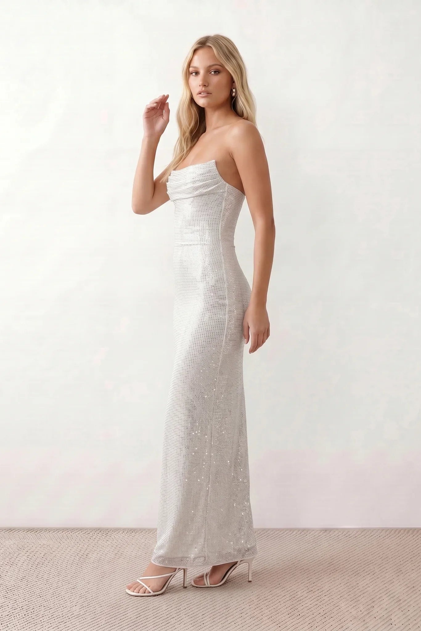 Woman wearing the Izabela sequined strapless maxi dress featuring shimmering all-over sequins, sparkling rhinestone embellishments, a ruched cowl-fold bust, adjustable lace-up corset back and a figure-skimming column silhouette with a floor-length hem, perfect for formal evening occasions.