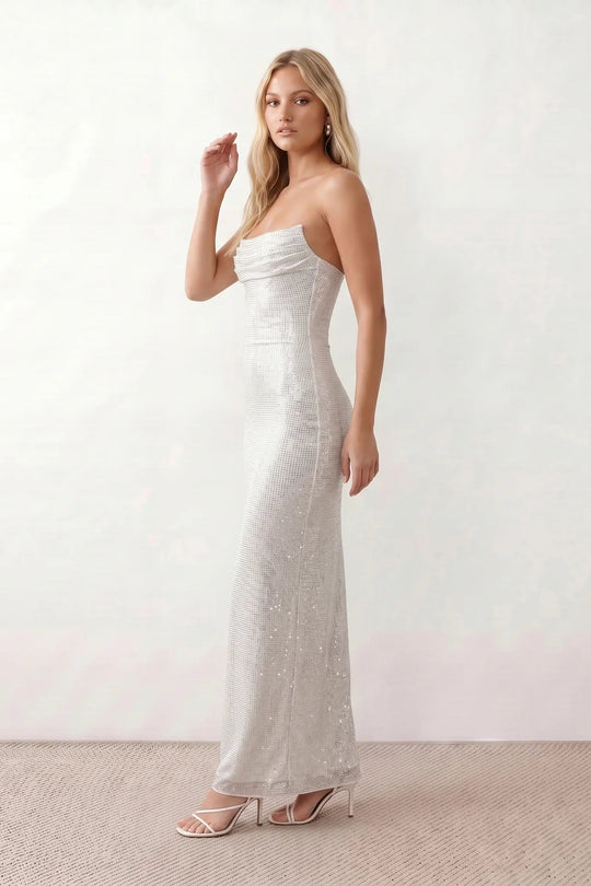 Woman wearing the Izabela sequined strapless maxi dress featuring shimmering all-over sequins, sparkling rhinestone embellishments, a ruched cowl-fold bust, adjustable lace-up corset back and a figure-skimming column silhouette with a floor-length hem, perfect for formal evening occasions.