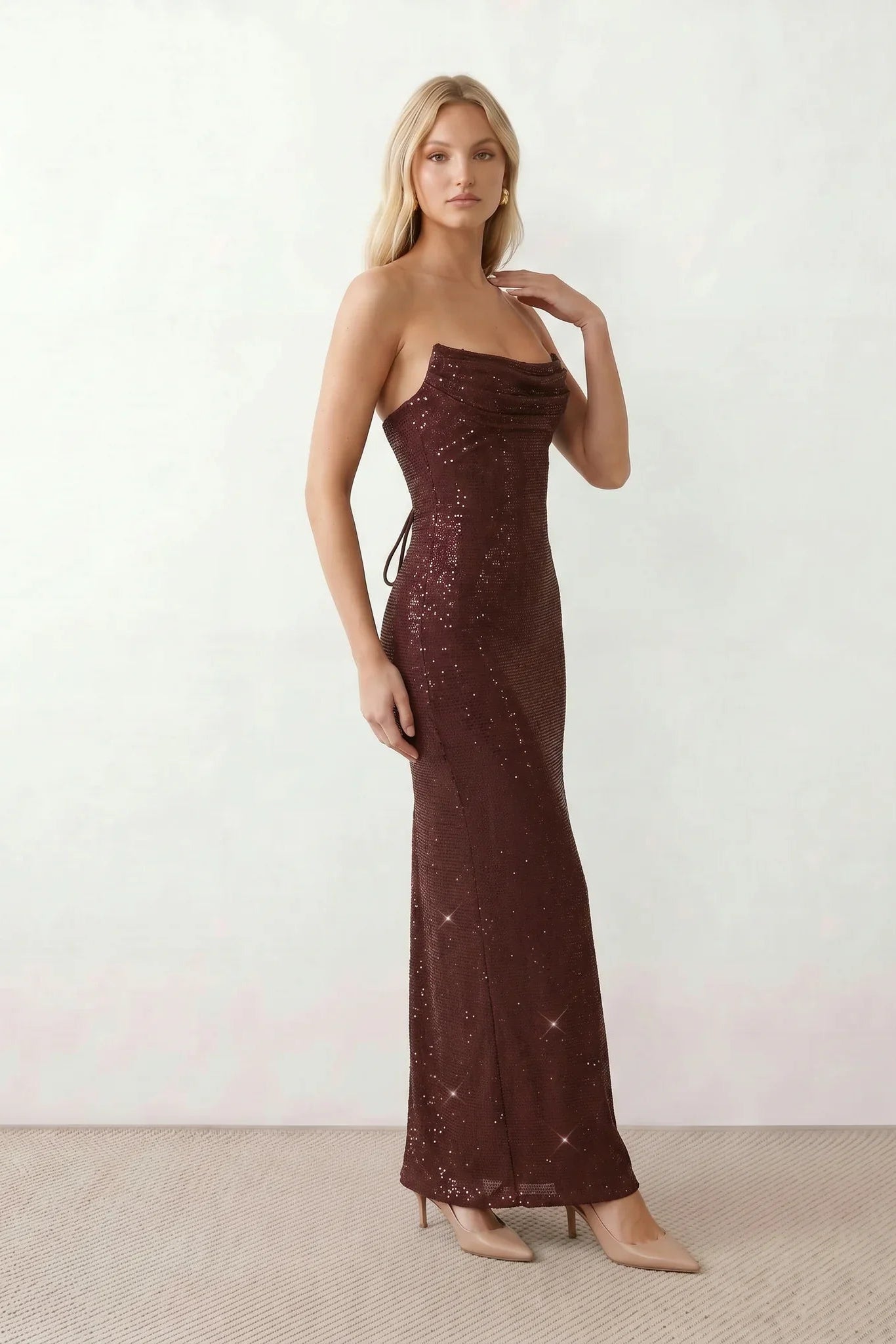 Woman wearing the Izabela sequined strapless maxi dress featuring shimmering all-over sequins, sparkling rhinestone embellishments, a ruched cowl-fold bust, adjustable lace-up corset back and a figure-skimming column silhouette with a floor-length hem, perfect for formal evening occasions.