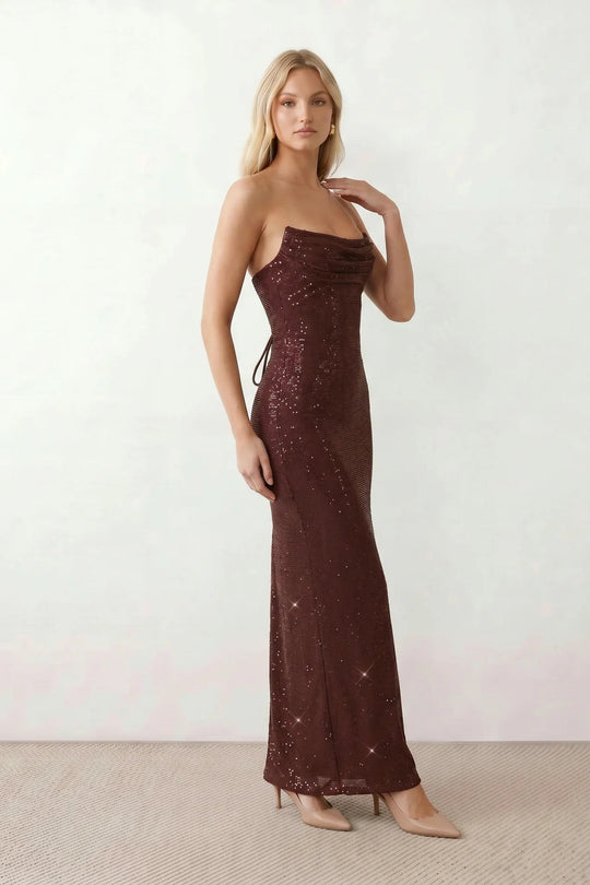 Woman wearing the Izabela sequined strapless maxi dress featuring shimmering all-over sequins, sparkling rhinestone embellishments, a ruched cowl-fold bust, adjustable lace-up corset back and a figure-skimming column silhouette with a floor-length hem, perfect for formal evening occasions.