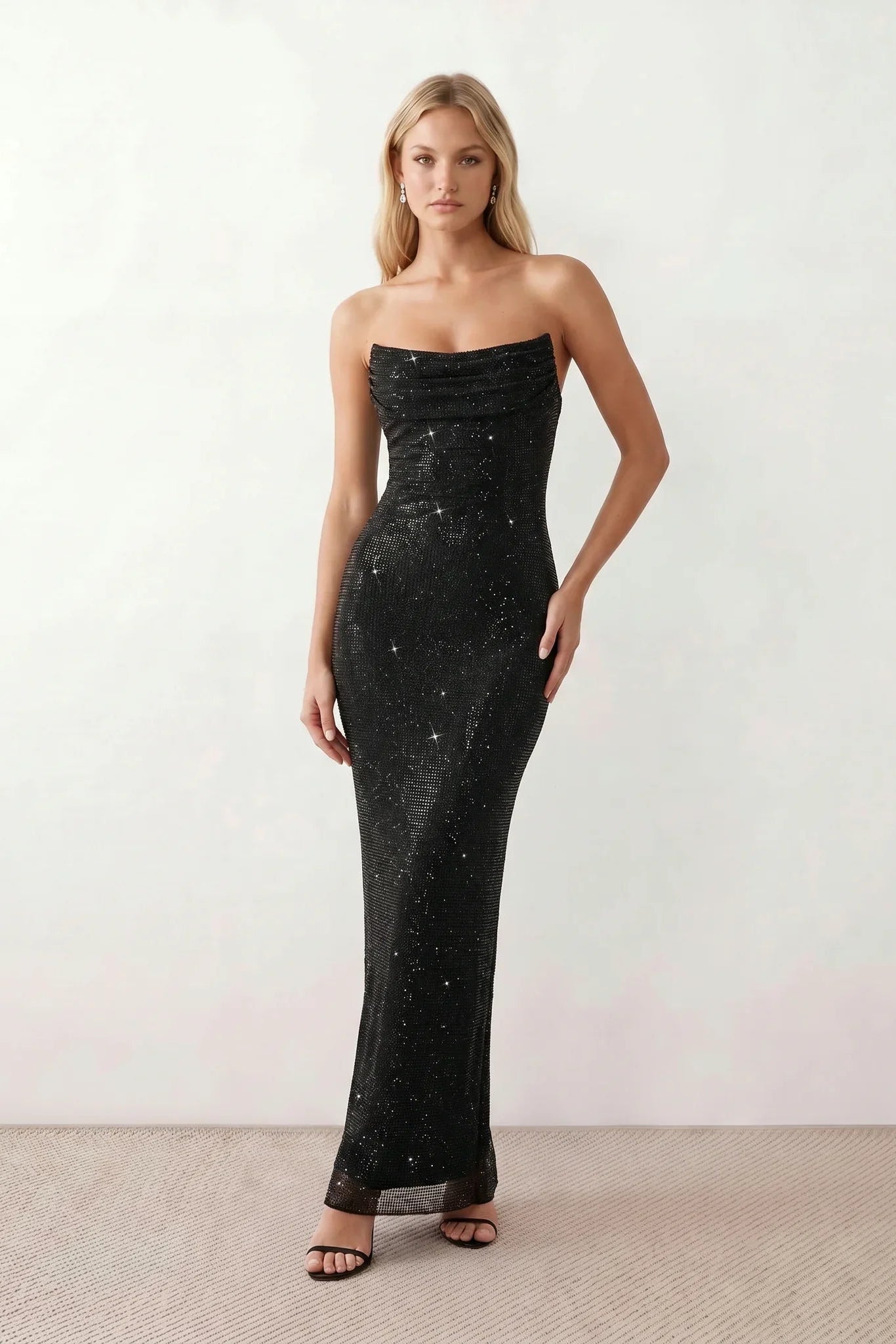 Woman wearing the Izabela sequined strapless maxi dress featuring shimmering all-over sequins, sparkling rhinestone embellishments, a ruched cowl-fold bust, adjustable lace-up corset back and a figure-skimming column silhouette with a floor-length hem, perfect for formal evening occasions.