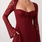 Woman wearing the Joaquina Lace Sweetheart Mini Dress in delicate lace-look fabric with a sweetheart neckline, long sleeves, an open lace-up back with bow detail, a defined waist and a flattering mini-length silhouette.