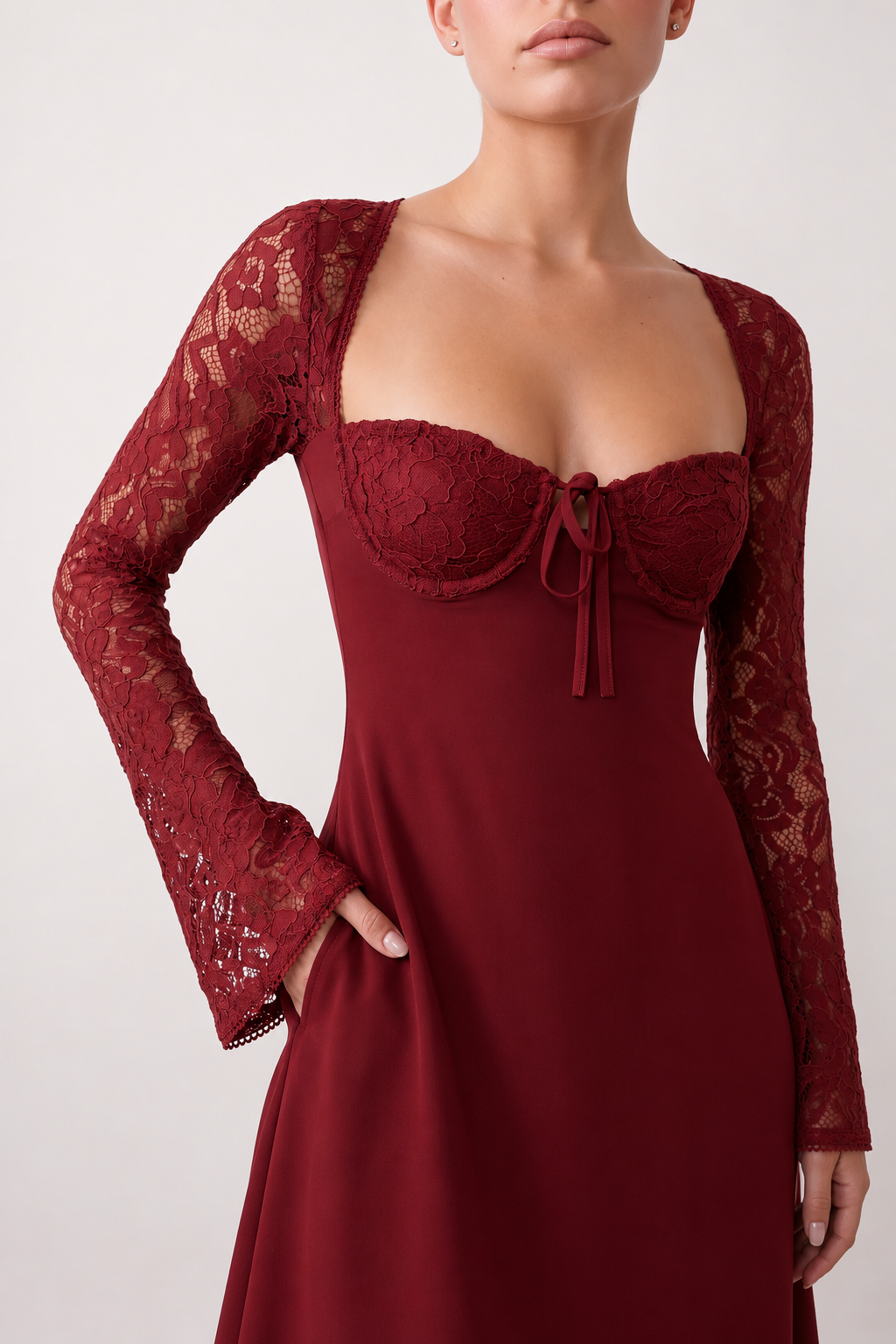 Woman wearing the Joaquina Lace Sweetheart Mini Dress in delicate lace-look fabric with a sweetheart neckline, long sleeves, an open lace-up back with bow detail, a defined waist and a flattering mini-length silhouette.