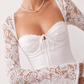Woman wearing the Joaquina Lace Sweetheart Mini Dress in delicate lace-look fabric with a sweetheart neckline, long sleeves, an open lace-up back with bow detail, a defined waist and a flattering mini-length silhouette.
