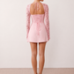 Woman wearing the Joaquina Lace Sweetheart Mini Dress in delicate lace-look fabric with a sweetheart neckline, long sleeves, an open lace-up back with bow detail, a defined waist and a flattering mini-length silhouette.