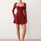 Woman wearing the Joaquina Lace Sweetheart Mini Dress in delicate lace-look fabric with a sweetheart neckline, long sleeves, an open lace-up back with bow detail, a defined waist and a flattering mini-length silhouette.