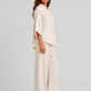Woman wearing a neutral linen blend two-piece set featuring a button-up shirt and relaxed wide-leg trousers, styled for effortless warm-weather elegance.