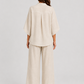 Woman wearing a neutral linen blend two-piece set featuring a button-up shirt and relaxed wide-leg trousers, styled for effortless warm-weather elegance.