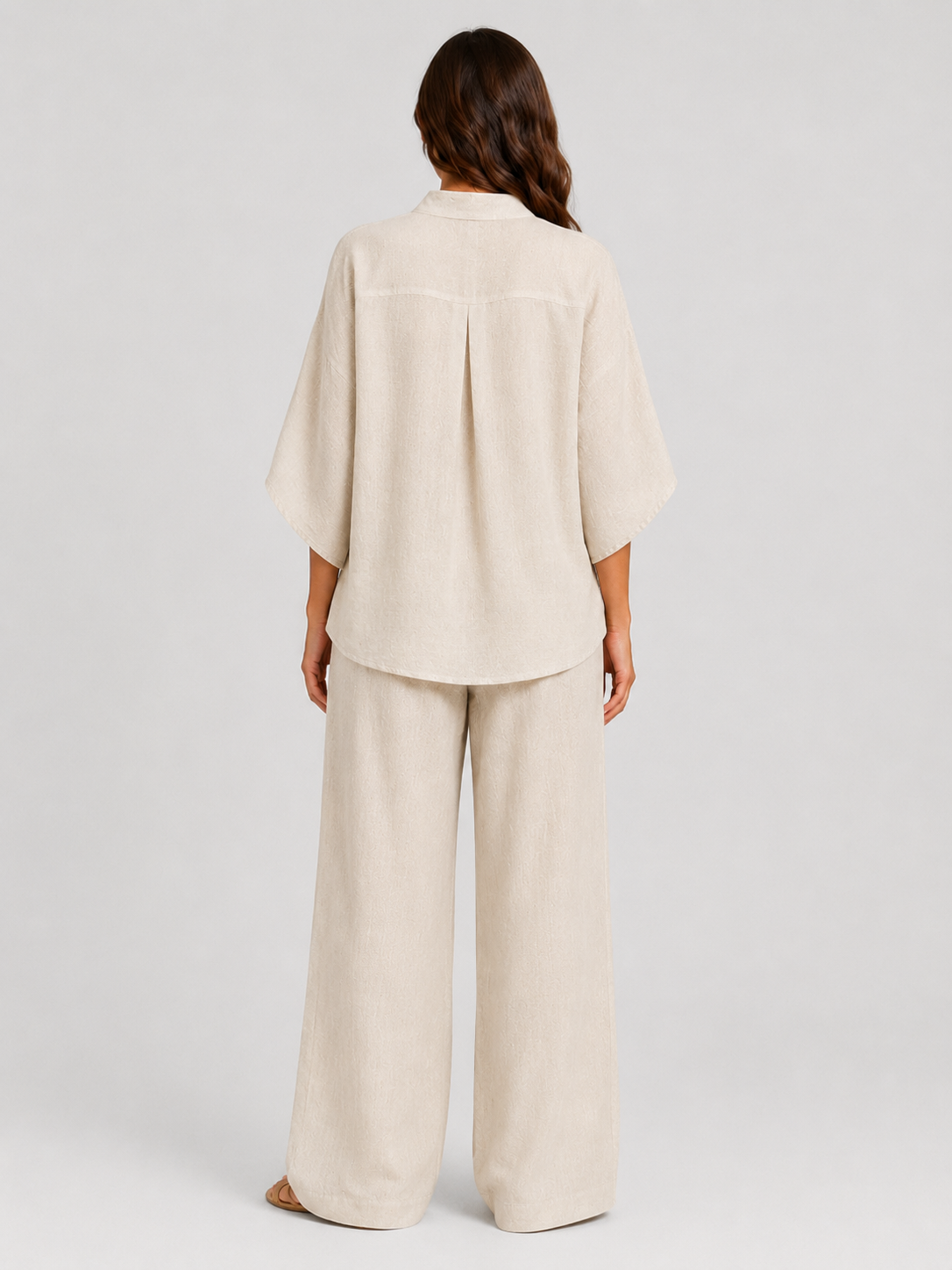 Woman wearing a neutral linen blend two-piece set featuring a button-up shirt and relaxed wide-leg trousers, styled for effortless warm-weather elegance.