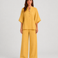 Woman wearing a neutral linen blend two-piece set featuring a button-up shirt and relaxed wide-leg trousers, styled for effortless warm-weather elegance.