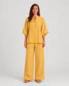Woman wearing a neutral linen blend two-piece set featuring a button-up shirt and relaxed wide-leg trousers, styled for effortless warm-weather elegance.