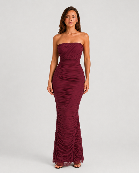 Woman wearing a strapless mesh maxi dress with internal corset detailing, elegant ruching, and a figure-hugging silhouette designed for formal evening occasions.