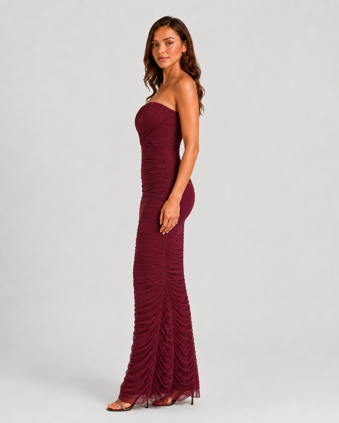 Woman wearing a strapless mesh maxi dress with internal corset detailing, elegant ruching, and a figure-hugging silhouette designed for formal evening occasions.