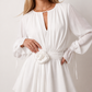 Woman wearing the Michela pleated tie detail mini dress featuring lightweight pleated fabric, a keyhole neckline with ribbon tie, billowy long sleeves with ribbon cuffs, a 3D floral corsage at the waist, belted sash, open low back and a double-layer ruffled hem, ideal for weddings, garden parties and special occasions.