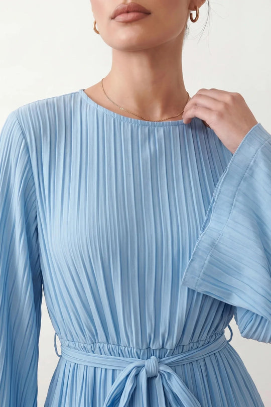 Woman wearing the Pleated Ruffle Detail Mini Dress featuring an all-over pleated design, flowing bell sleeves, a round neckline, elasticated waist with a self-tie sash, and a feminine ruffle hem, perfect for weddings, garden parties, race days, and elegant occasions.