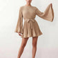 Woman wearing the Pleated Ruffle Detail Mini Dress featuring an all-over pleated design, flowing bell sleeves, a round neckline, elasticated waist with a self-tie sash, and a feminine ruffle hem, perfect for weddings, garden parties, race days, and elegant occasions.
