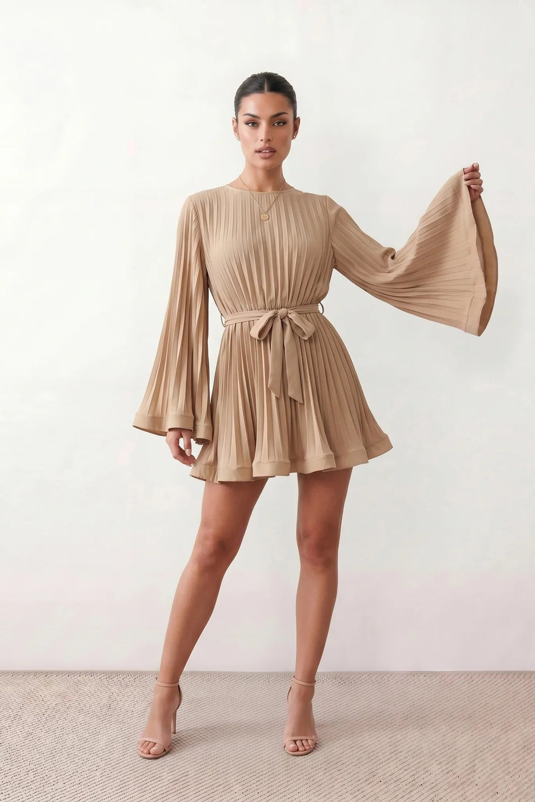 Woman wearing the Pleated Ruffle Detail Mini Dress featuring an all-over pleated design, flowing bell sleeves, a round neckline, elasticated waist with a self-tie sash, and a feminine ruffle hem, perfect for weddings, garden parties, race days, and elegant occasions.