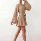Woman wearing the Pleated Ruffle Detail Mini Dress featuring an all-over pleated design, flowing bell sleeves, a round neckline, elasticated waist with a self-tie sash, and a feminine ruffle hem, perfect for weddings, garden parties, race days, and elegant occasions.