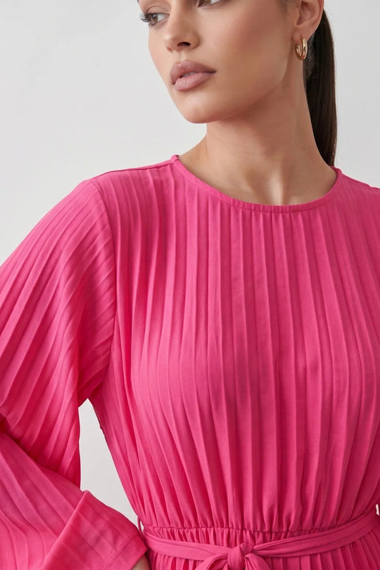 Woman wearing the Pleated Ruffle Detail Mini Dress featuring an all-over pleated design, flowing bell sleeves, a round neckline, elasticated waist with a self-tie sash, and a feminine ruffle hem, perfect for weddings, garden parties, race days, and elegant occasions.