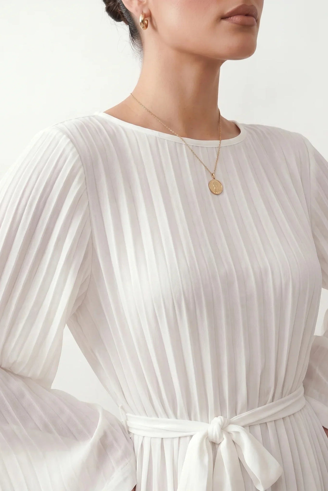 Woman wearing the Pleated Ruffle Detail Mini Dress featuring an all-over pleated design, flowing bell sleeves, a round neckline, elasticated waist with a self-tie sash, and a feminine ruffle hem, perfect for weddings, garden parties, race days, and elegant occasions.