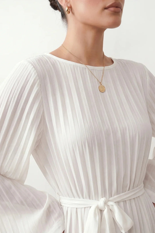 Woman wearing the Pleated Ruffle Detail Mini Dress featuring an all-over pleated design, flowing bell sleeves, a round neckline, elasticated waist with a self-tie sash, and a feminine ruffle hem, perfect for weddings, garden parties, race days, and elegant occasions.