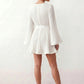 Woman wearing the Pleated Ruffle Detail Mini Dress featuring an all-over pleated design, flowing bell sleeves, a round neckline, elasticated waist with a self-tie sash, and a feminine ruffle hem, perfect for weddings, garden parties, race days, and elegant occasions.