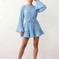 Woman wearing the Pleated Ruffle Detail Mini Dress featuring an all-over pleated design, flowing bell sleeves, a round neckline, elasticated waist with a self-tie sash, and a feminine ruffle hem, perfect for weddings, garden parties, race days, and elegant occasions.