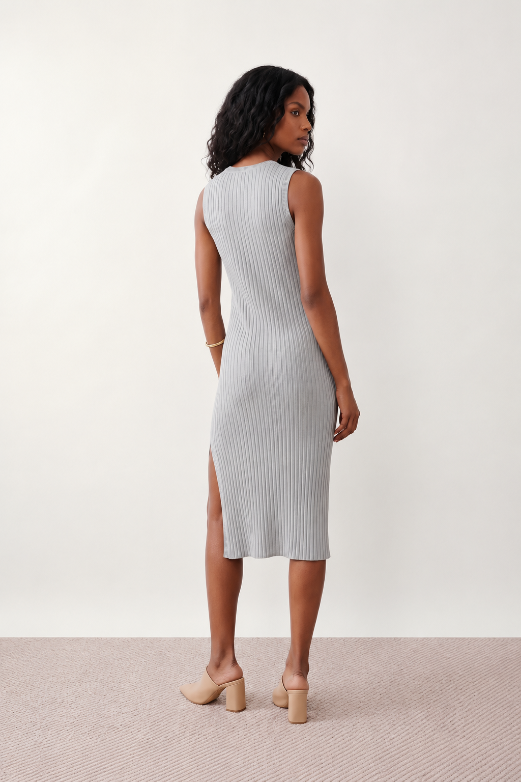 Woman wearing the Raina ribbed fitted midi dress in a sleeveless bodycon design with a round neckline, wide-rib knit texture and elegant side slit, styled as a sophisticated occasion dress.