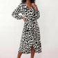 Woman wearing the Rosa Animal Print Wrap Front Midi Dress in a flowing leopard print fabric, featuring a wrap-front V-neckline, adjustable self-tie waist, long sleeves with gathered elasticated cuffs, a high-low midi hem, and a front slit, styled for weddings, cocktail parties, and elegant occasions.