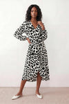 Woman wearing the Rosa Animal Print Wrap Front Midi Dress in a flowing leopard print fabric, featuring a wrap-front V-neckline, adjustable self-tie waist, long sleeves with gathered elasticated cuffs, a high-low midi hem, and a front slit, styled for weddings, cocktail parties, and elegant occasions.