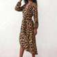 Woman wearing the Rosa Animal Print Wrap Front Midi Dress in a flowing leopard print fabric, featuring a wrap-front V-neckline, adjustable self-tie waist, long sleeves with gathered elasticated cuffs, a high-low midi hem, and a front slit, styled for weddings, cocktail parties, and elegant occasions.