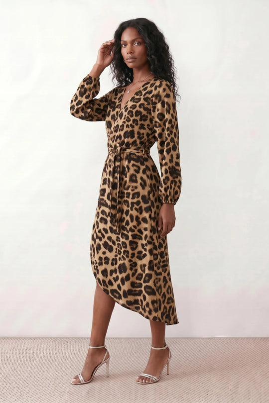 Woman wearing the Rosa Animal Print Wrap Front Midi Dress in a flowing leopard print fabric, featuring a wrap-front V-neckline, adjustable self-tie waist, long sleeves with gathered elasticated cuffs, a high-low midi hem, and a front slit, styled for weddings, cocktail parties, and elegant occasions.