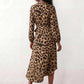 Woman wearing the Rosa Animal Print Wrap Front Midi Dress in a flowing leopard print fabric, featuring a wrap-front V-neckline, adjustable self-tie waist, long sleeves with gathered elasticated cuffs, a high-low midi hem, and a front slit, styled for weddings, cocktail parties, and elegant occasions.