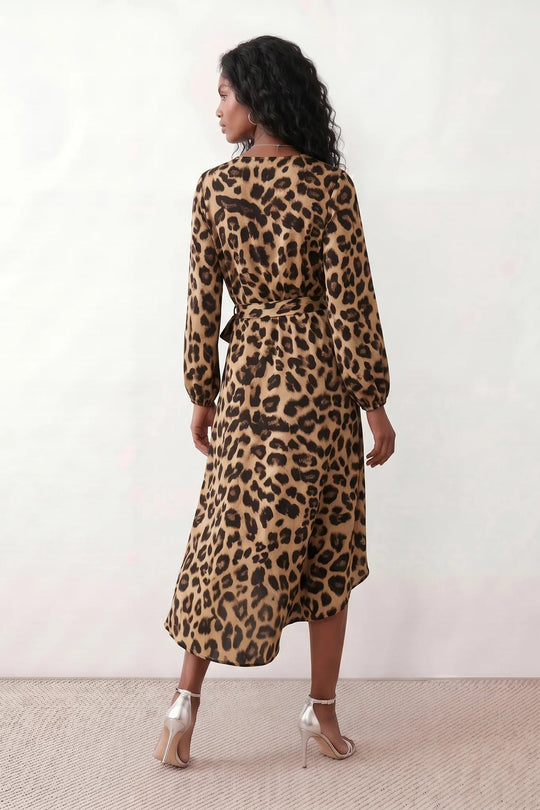 Woman wearing the Rosa Animal Print Wrap Front Midi Dress in a flowing leopard print fabric, featuring a wrap-front V-neckline, adjustable self-tie waist, long sleeves with gathered elasticated cuffs, a high-low midi hem, and a front slit, styled for weddings, cocktail parties, and elegant occasions.