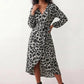 Woman wearing the Rosa Animal Print Wrap Front Midi Dress in a flowing leopard print fabric, featuring a wrap-front V-neckline, adjustable self-tie waist, long sleeves with gathered elasticated cuffs, a high-low midi hem, and a front slit, styled for weddings, cocktail parties, and elegant occasions.