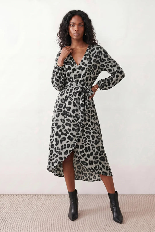 Woman wearing the Rosa Animal Print Wrap Front Midi Dress in a flowing leopard print fabric, featuring a wrap-front V-neckline, adjustable self-tie waist, long sleeves with gathered elasticated cuffs, a high-low midi hem, and a front slit, styled for weddings, cocktail parties, and elegant occasions.