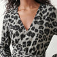 Woman wearing the Rosa Animal Print Wrap Front Midi Dress in a flowing leopard print fabric, featuring a wrap-front V-neckline, adjustable self-tie waist, long sleeves with gathered elasticated cuffs, a high-low midi hem, and a front slit, styled for weddings, cocktail parties, and elegant occasions.