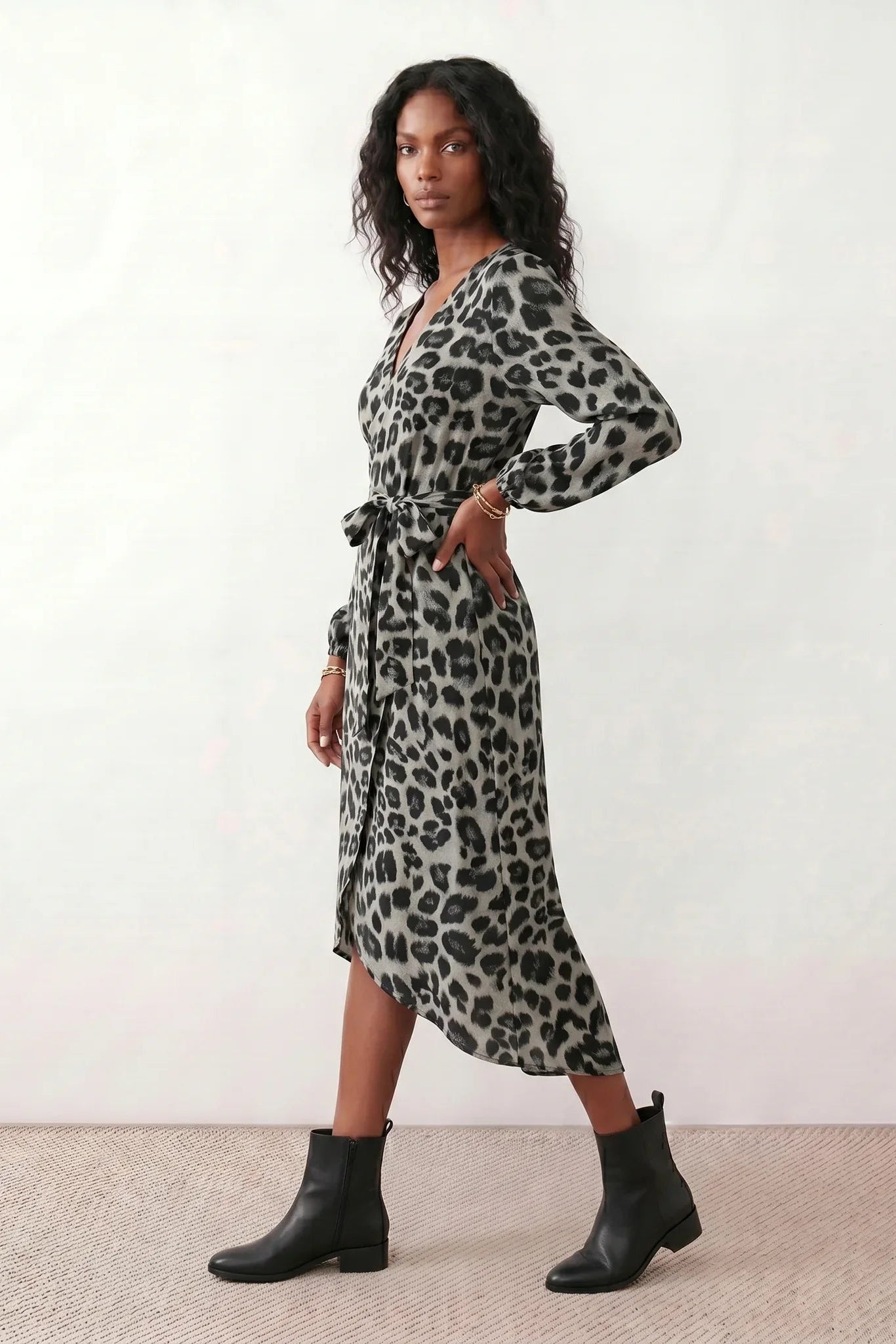 Woman wearing the Rosa Animal Print Wrap Front Midi Dress in a flowing leopard print fabric, featuring a wrap-front V-neckline, adjustable self-tie waist, long sleeves with gathered elasticated cuffs, a high-low midi hem, and a front slit, styled for weddings, cocktail parties, and elegant occasions.