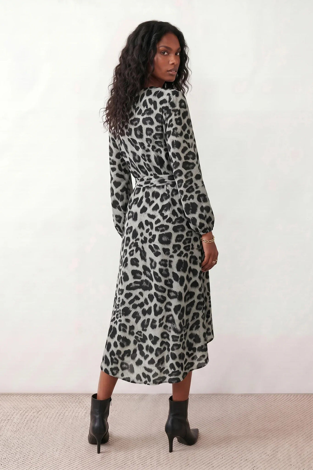 Woman wearing the Rosa Animal Print Wrap Front Midi Dress in a flowing leopard print fabric, featuring a wrap-front V-neckline, adjustable self-tie waist, long sleeves with gathered elasticated cuffs, a high-low midi hem, and a front slit, styled for weddings, cocktail parties, and elegant occasions.