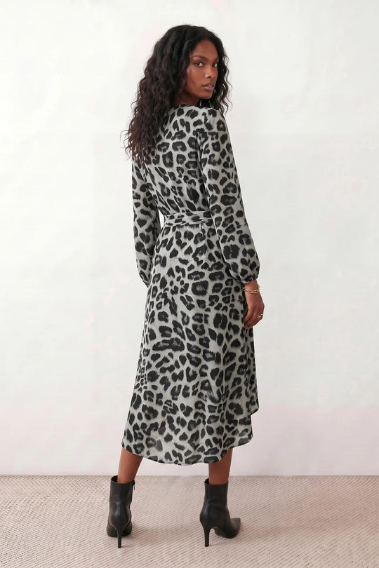 Woman wearing the Rosa Animal Print Wrap Front Midi Dress in a flowing leopard print fabric, featuring a wrap-front V-neckline, adjustable self-tie waist, long sleeves with gathered elasticated cuffs, a high-low midi hem, and a front slit, styled for weddings, cocktail parties, and elegant occasions.