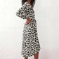 Woman wearing the Rosa Animal Print Wrap Front Midi Dress in a flowing leopard print fabric, featuring a wrap-front V-neckline, adjustable self-tie waist, long sleeves with gathered elasticated cuffs, a high-low midi hem, and a front slit, styled for weddings, cocktail parties, and elegant occasions.